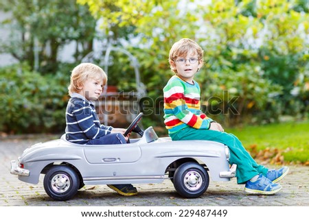 Two happy kids playing with big old toy car in summer garden, outdoors. Twins boys and friends on warm day.
