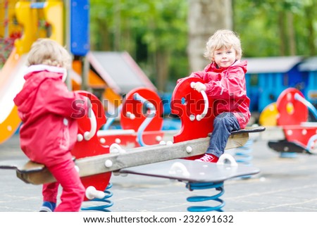 Two little sibling kid boys playing together on a playground, outdoors in summer. on a rainy day, selective focus on one boy