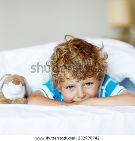 Adorable kid boy after sleeping in his white bed with toy. Square format.