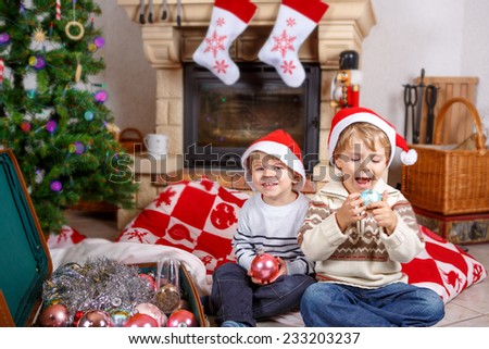 Two little sibling boys playing with christmas toys, indoor with christmas decoration. Family celebrating holiday together.