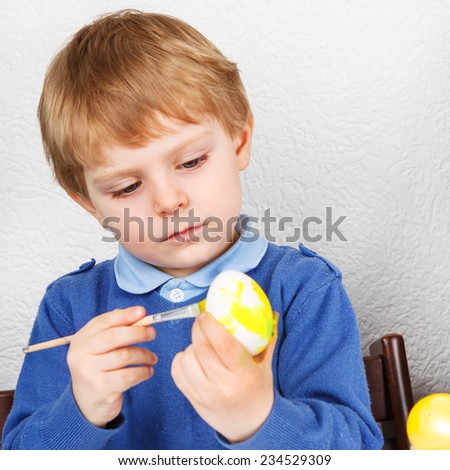 Little toddler boy painting colorful eggs for Easter hunt, traditional action in Germany for Eastern holiday, indoors. Square format.