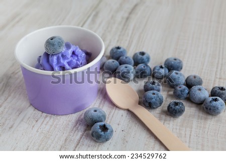 Serving of ice cream  with whole fresh blueberries and yoghurt. With wooden spoon and with selective focus. Healthy sweet dessert with organic berries.