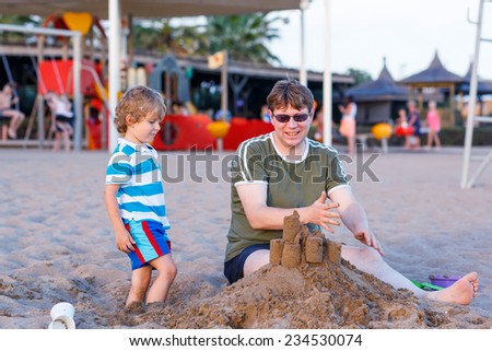 Happy father and and little son building sand castle on  sand beach by sundown