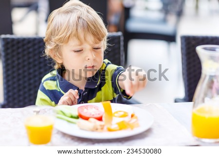 Little kid boy having healthy breakfast in hotel restaurant or city cafe.