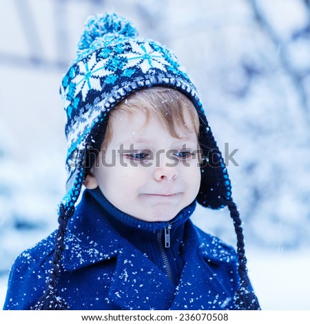 cute little child in winter clothes with falling snow. Kid enjoying and catching snowflakes, outdoors on cold day. Square format.