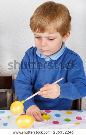 Little toddler boy painting colorful eggs for Easter hunt, traditional action in Germany for Eastern holiday, indoors