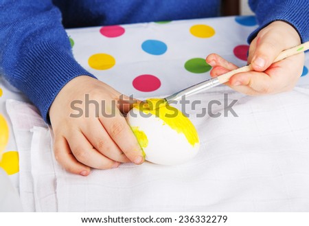 Hands of toddler boy painting colorful eggs for Easter hunt, traditional action in Germany for Eastern holiday, indoors