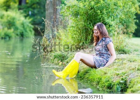 Young beautiful woman sitting in yellow rain rubber boats by a river in summer.