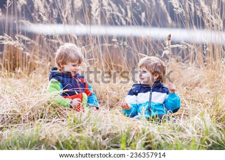 Two little sibling boys fighting and having fun with bulrush near forest lake, nature on cold spring or autumn day.