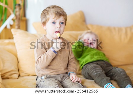 Two little brother boys watching tv and eating candy indoor. Selective focus on child on foreground. Kids fun at home.