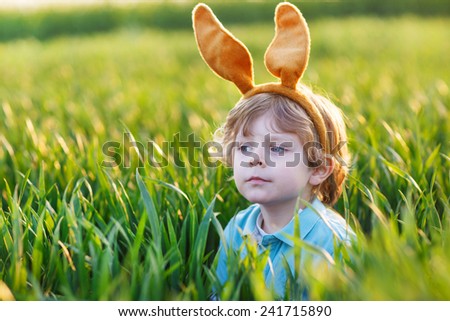 Cute little child with Easter bunny ears playing in green grass on sunny spring day, celebrating Easter holiday
