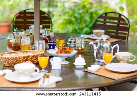 Table laid for breakfast outside in summer with various jams, bread, coffee, croissants, muesli and orange juice. French breakfast. Provence, France
