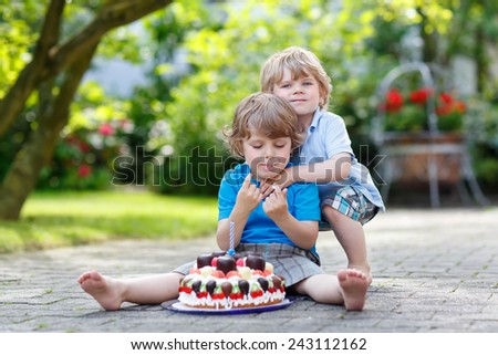 Funny cute kid celebrating his third birthday in home\'s garden with big cake. His brother hugging him. Two little children having fun together.