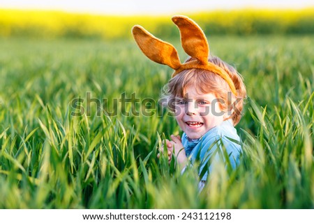 Cute little kid boy with Easter bunny ears  in green grass on Easter holiday. Celebrating traditional european feast and making egg hunt. On warm spring day.