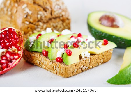 Avocado with Feta, pomegranate and olive oil on sunflower seeds bread sandwich. Healthy organic and vegan breakfast, on white wooden background