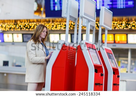 Young woman at international airport, checking in on electronic terminal waiting for her flight. Female passenger at terminal, indoors.