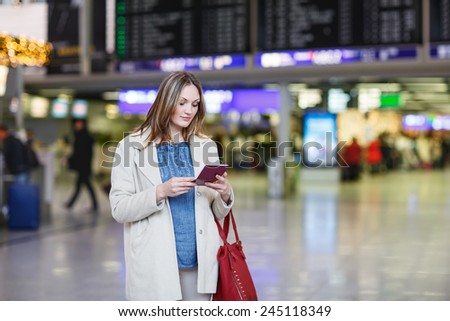 Young woman  at international airport, checking electronic board, holding passport and ticket and waiting for her flight. Female passenger at terminal, indoors.
