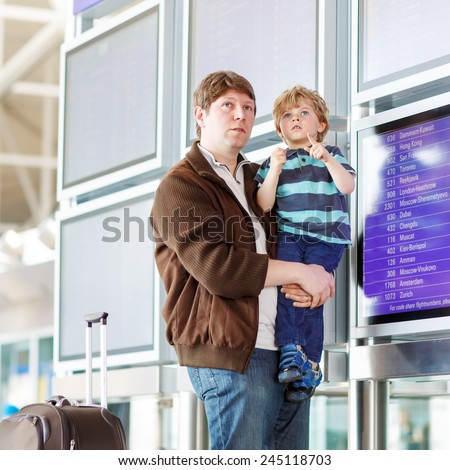 Happy family of two: Father and little son at the international airport, looking on flight board at terminal, going on vacation. Ready for take off.