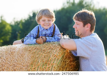 Young father and his little son having fun on yellow hay field in summer. Happy family of two. Active outdoors leisure with children on warm summer day.