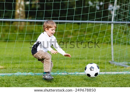 Adorable cute little kid boy playing soccer and football and having fun, outdoors on field. Active leisure with children on warm sunny summer day.