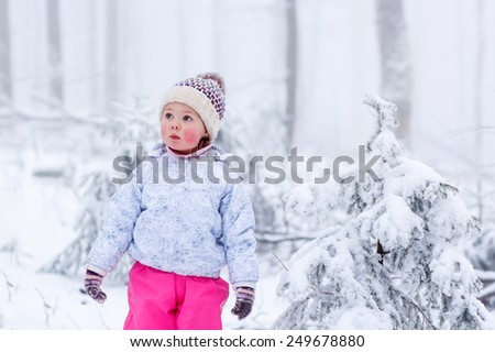 portrait of a little girl in winter hat in snow forest at snowflakes background. outdoors winter leisure and lifestyle with kids.