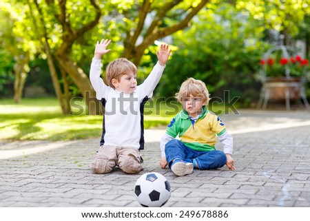 Two little sibling boys playing soccer and football and having fun, outdoors. Active leisure with children on warm sunny summer day.