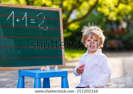 Happy cute child at blackboard practicing mathematics, outdoor school or nursery.
