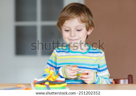 Active and creative kid boy playing with dough, colorful modeling compound, sitting at table at home or school. Creative leisure with kids.