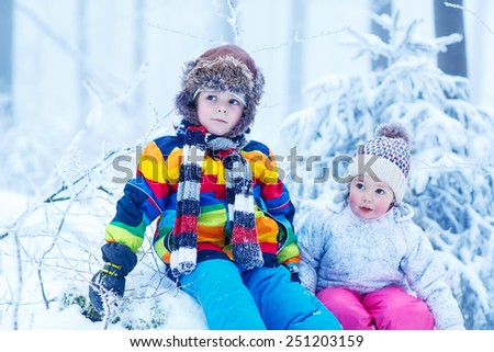 portrait of two kids: boy and girl in winter hat in snow forest at snowflakes background. outdoors winter leisure and lifestyle with children on cold days.