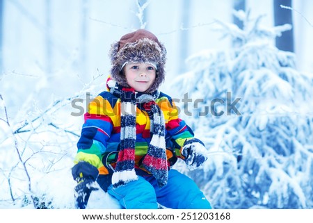 Winter portrait of kid boy in colorful winter clothes, outdoors during snowfall. Active outoors leisure with children in winter on cold snowy days