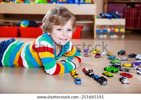 Funny little boy playing with lots of toy cars indoor, at home or at nursery. Kid boy wearing colorful shirt and having fun.
