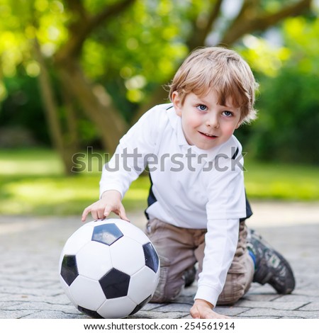Active cute little kid boy playing soccer and football and having fun, outdoors. Active leisure with children on warm sunny summer day.