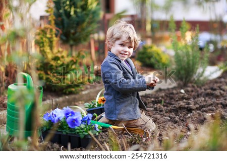 Blond boy of 2 years having fun with gardening and planting vegetable plants and flowers in garden, outdoors. Active leisure with kids, learning gardening and environment.