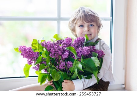 Adorable smiling little boy with blooming purple lilac flowers, indoor. Mother\'s day, father\'s day or valentine\'s day concept.