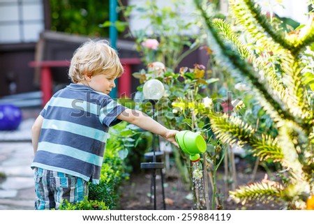 Little blond kid boy playing with water can toy in summer garden. On warm summer day, happy leisure with children outdoors.