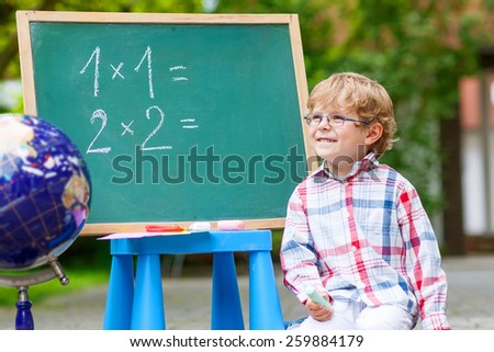 Funny little kid with glasses at blackboard practicing mathematics, outdoor. school or nursery. Back to school concept for little children