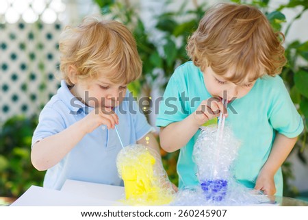 Two little boys making experiment with colorful soap bubbles and water, outdoors. Creative leisure for little kids with water and soap.
