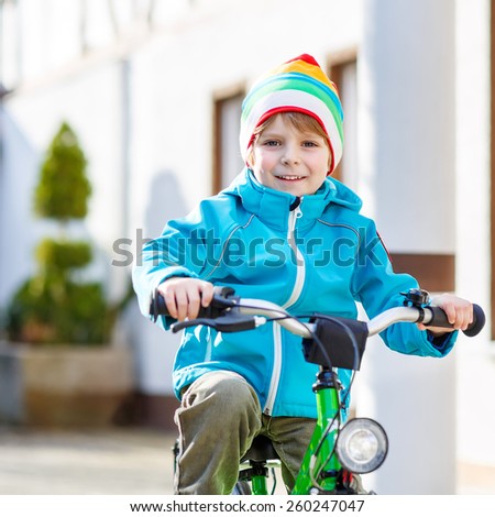 Cute kid boy riding with his first green bike in the city. Happy child in colorful clothes. Active leisure for kids outdoors.
