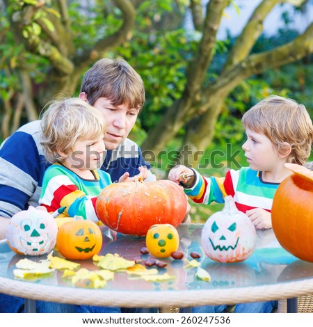Young dad and his two little sons making jack-o-lantern for halloween in autumn garden, outdoors. Family having fun together