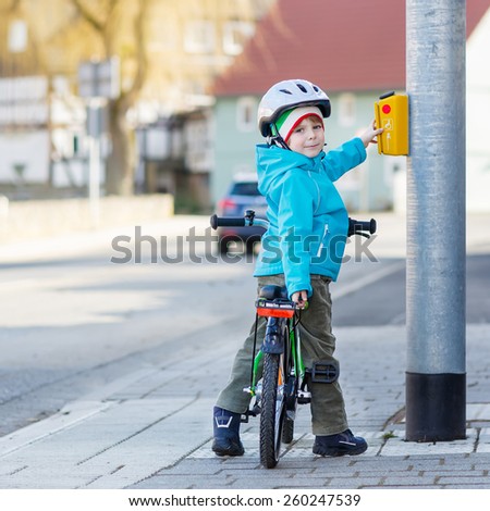 Smiling kid boy of 5 years riding with his first green bike in the city. Happy child in colorful clothes standing near traffic lights. Active leisure for kids outdoors.