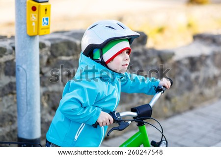 Little preschool kid boy riding with his first green bike in the city. Happy child in colorful clothes standing and waiting near traffic lights. Active leisure for kids outdoors.