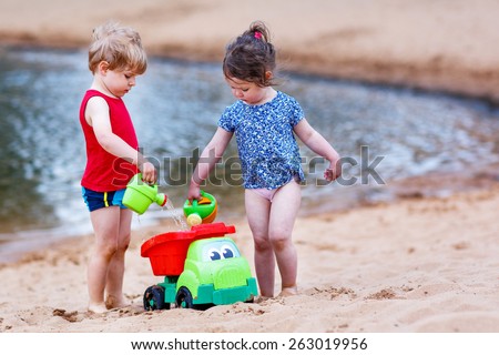 Little brother and sister playing together with sand toys near city lake on hot summer day. Active outdoors leisure with kids in summer, on sunny day.