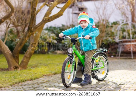 Little preschool kid boy riding with his first green bike in the city. Happy child in colorful clothes. Active leisure for kids outdoors.