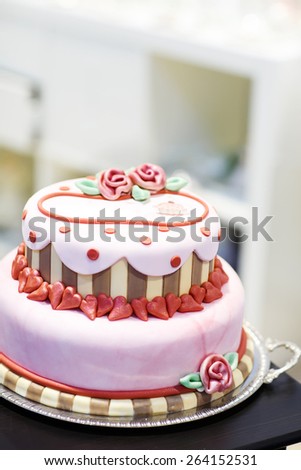 Beautiful wedding cake in different colors with two levels and marzipan roses. Icing with cream, marzipan, details of cake.