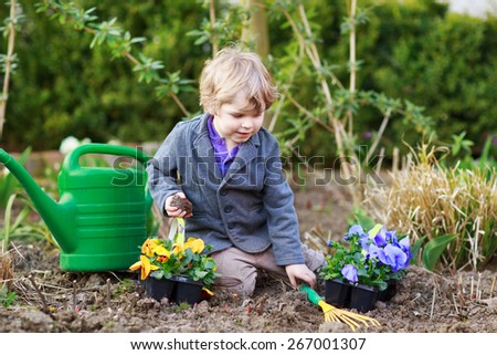Blond boy of 2 years having fun with gardening and planting vegetable plants and flowers in garden, outdoors