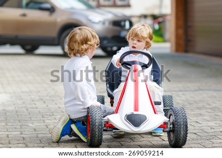 Two happy brothers boys playing with toy car in summer garden, outdoors. Kids having fun in domestic garden or nursery on sunny warm day.