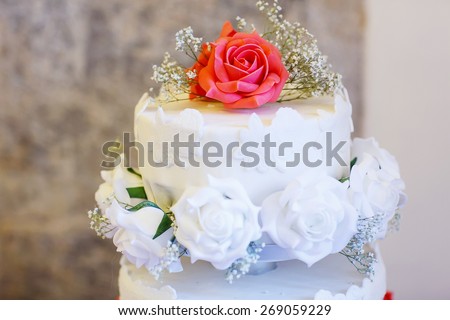 Beautiful wedding cake in different colors with two levels and marzipan roses. Icing with cream, marzipan, details of cake.