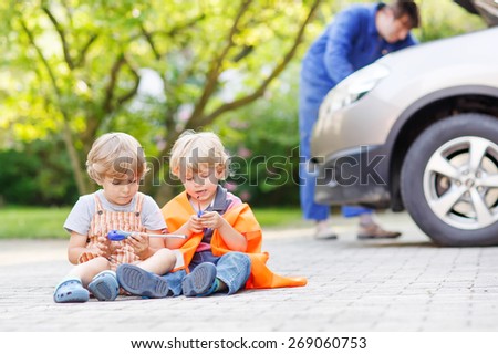 Two little kid boys in orange safety vest during their dad repairing family car on background