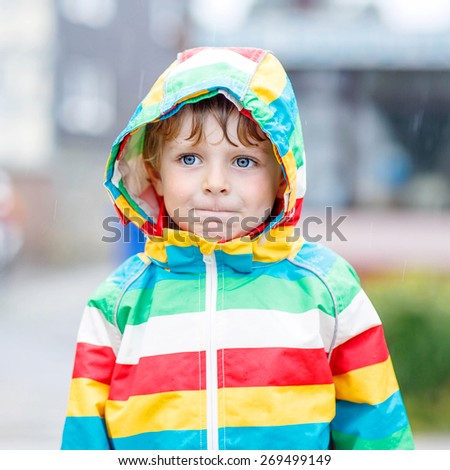 Portrait of funny boy on a rainy day. Child with blue eyes and wet blond hairs wearing rain jacket.