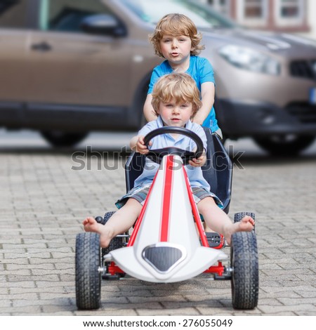 Two happy little boy friends having fun with toy race car in summer garden, outdoors. Active kid pushing the car with younger boy. Outdoor games for children in summer concept.
